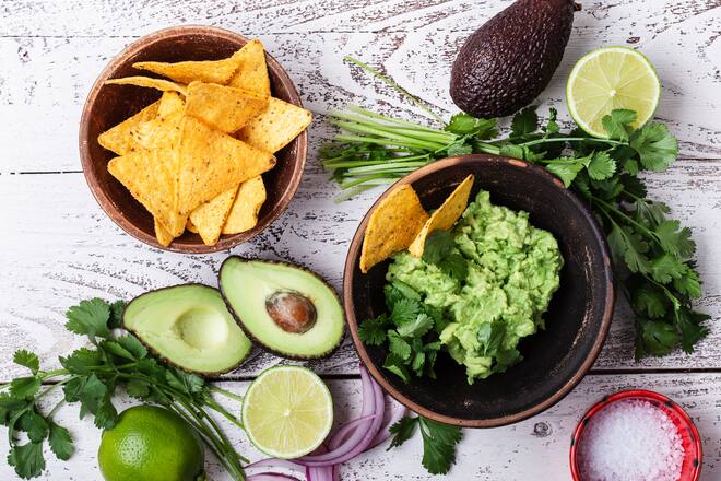 Making guacamole sauce, avocado, cilantro, lime, pepper, salt, tortilla corn chips. Mexican cuisine ingredients on rustic wooden background, top view