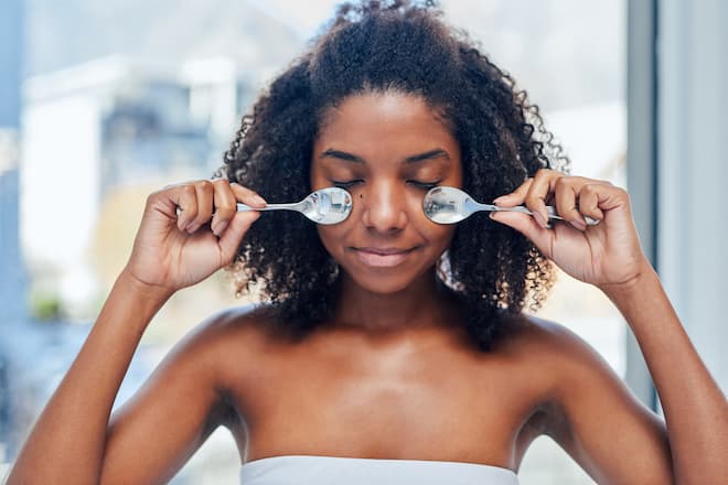 Shot of a young woman massaging her eyes with two teaspoons