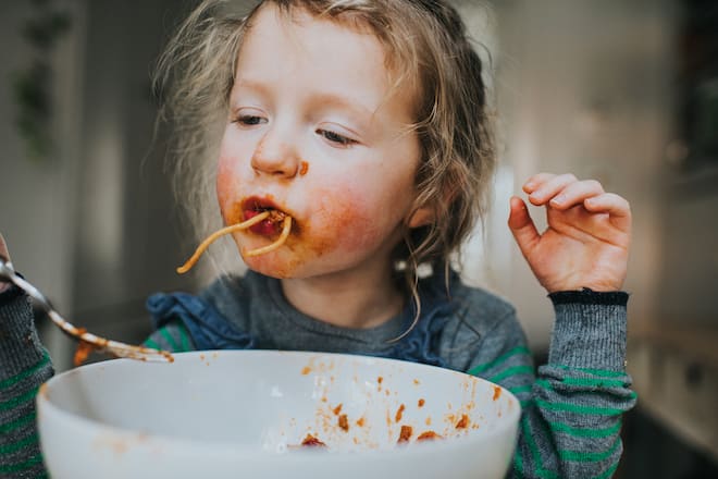 Cute young girl messily eating a big white bowl of Spaghetti Bolognese.