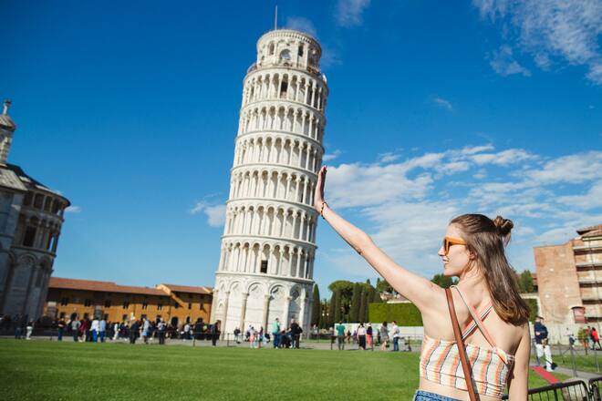 A woman is gesturing with her hands in front of the Leaning Tower of Pisa.