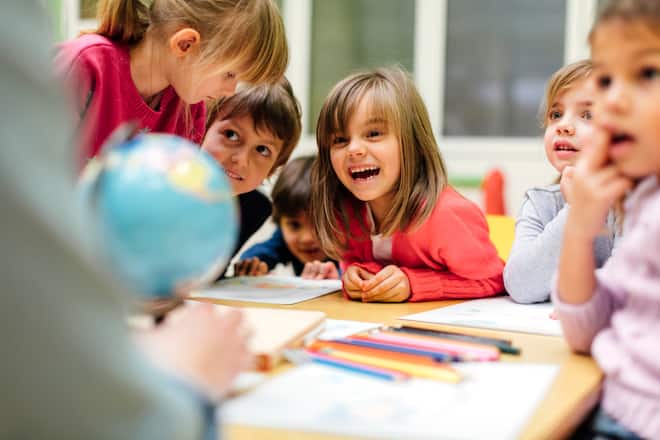 Preschool teacher teaching her children about geography. Using globe and asking the questions. Children sitting by the table and listen teacher carefully. Models in this shot are part of real kindergarten group and their teacher.
