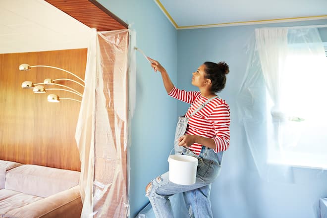 Pregnant young woman holding bucket while applying paint on wall at home