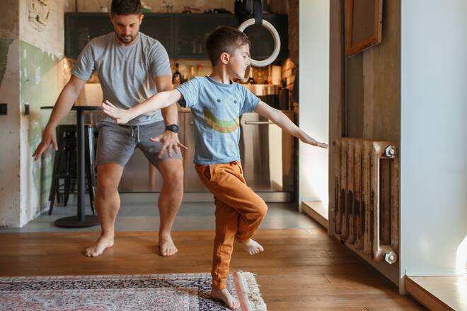 A little boy and his father are fooling around at home. They dance in the kitchen