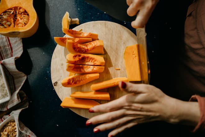 Caucasian woman slicing a Butternut Squash on a wooden cutting board. High view
