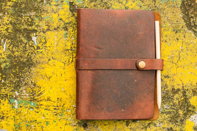 Flat lay of leather-bound personal organizer notepad on a weathered vibrant yellow paint background