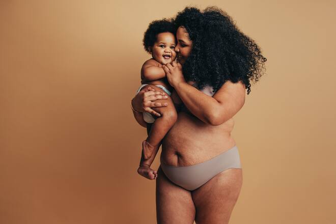Plus size woman with her baby. Happy mother carrying her toddler in studio. Real woman body after child birth.