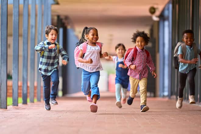 Group Of Multi-Cultural Elementary School Pupils Running Along Walkway Outdoors At School