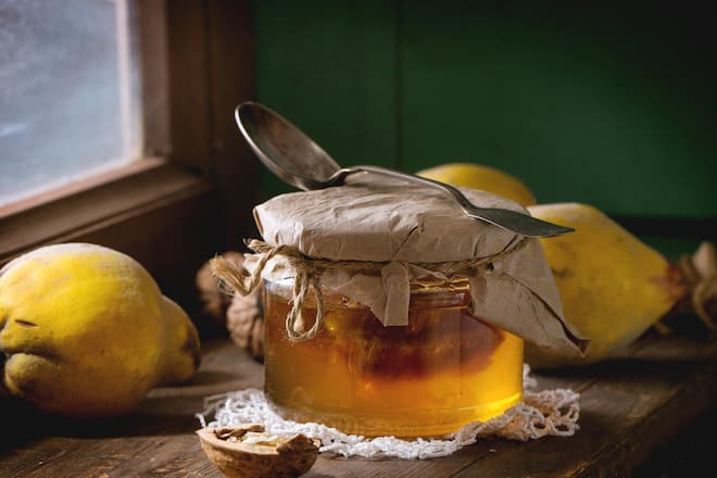 Three juicy quinces, walnuts and jar of honey over wooden table near window with bright sunlight. With green wooden wall at background. Dark rustic style.