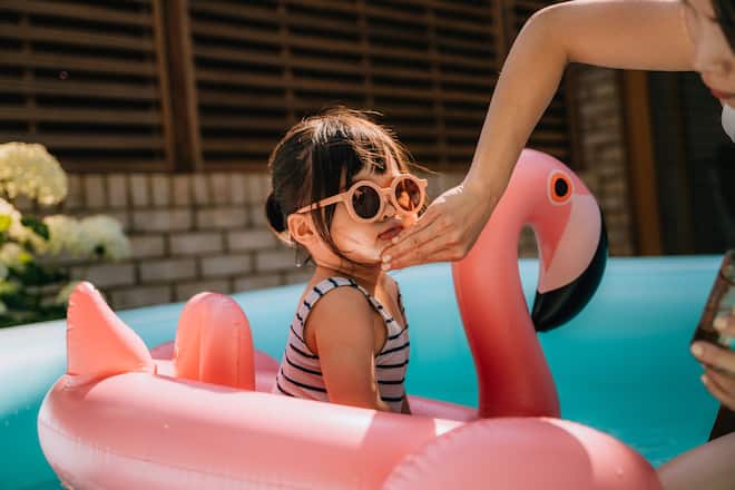 Caring mother putting suncream on her daughter's face while playing in swimming pool. Skincare and beauty.