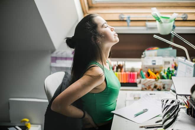 hispanic young woman having back pain while sitting on desk .She is working at home .Environment home
