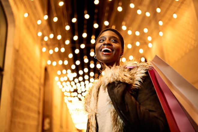 Young African American woman joyfully shopping at night with festive Christmas lights