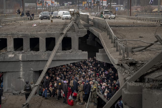 Ukrainians huddle under a destroyed bridge as they try to flee by crossing the Irpin River on the outskirts of Kyiv, Ukraine, on March 5, 2022. (AP Photo/Emilio Morenatti)