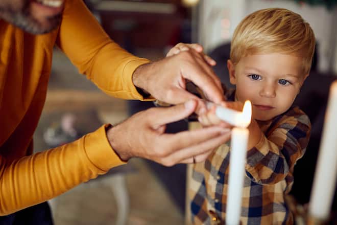 Unrecognizable Jewish father and his son lighting up traditional Hanukkah candles at home.