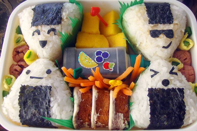 Bento box lunch consisting of four triangular onigiri with cute faces, mango, and mini carrot cakes.