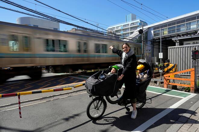 Sandra Tanaka is portrayed sitting on her electric power-assisted bicycle with child seats before a railroad crossing in her neighborhood in Tokyo, Japan, 09 March 2024. Lio Tanaka is 3 years old Levi Tanaka is 1 year old Yusuke Tanaka is 34 years old Sandra Tanaka is 32 years old
