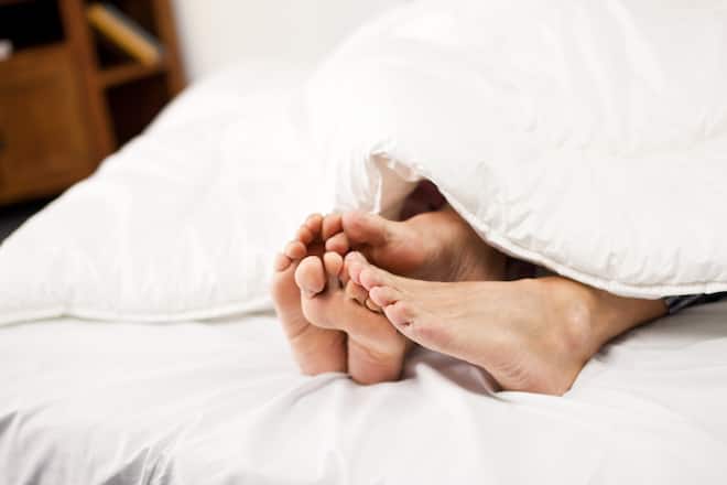 Mature couple showing feet from under the covers.