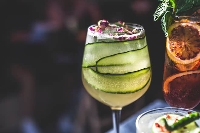 A pair of fresh cocktails on the marble counter top of a bar, glittering in the sunlight.