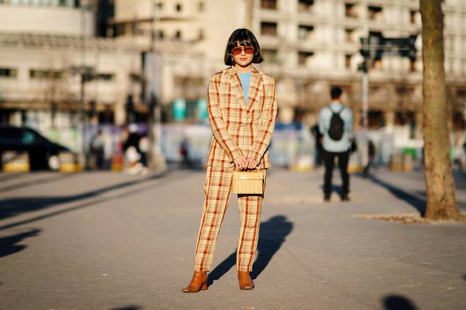 PARIS, FRANCE - FEBRUARY 26: A guest wears sunglasses, earrings, a light brown checkered pantsuit, a blue sweater, a Wicker Wings rattan bag, gold leather boots , outside Koche, during Paris Fashion Week Womenswear Fall/Winter 2019/2020, on February 26, 2019 in Paris, France. (Photo by Edward Berthelot/Getty Images)