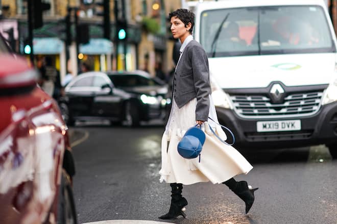 LONDON, ENGLAND - SEPTEMBER 16: Yasmin Sewell wears a gray jacket, a white dress, black boots, a blue bag shaped as a cap hat, during London Fashion Week September 2019 on September 16, 2019 in London, England. (Photo by Edward Berthelot/Getty Images)