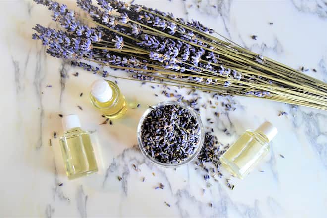 Aromatic oils with lavender flowers on marble background, seen from above