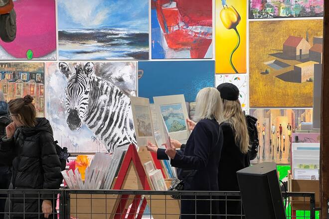 two persons looking at images in an exhibition with many paintings on the wall