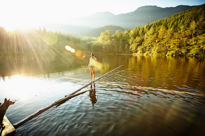 Woman walking on log in alpine lake with dog watching from dock