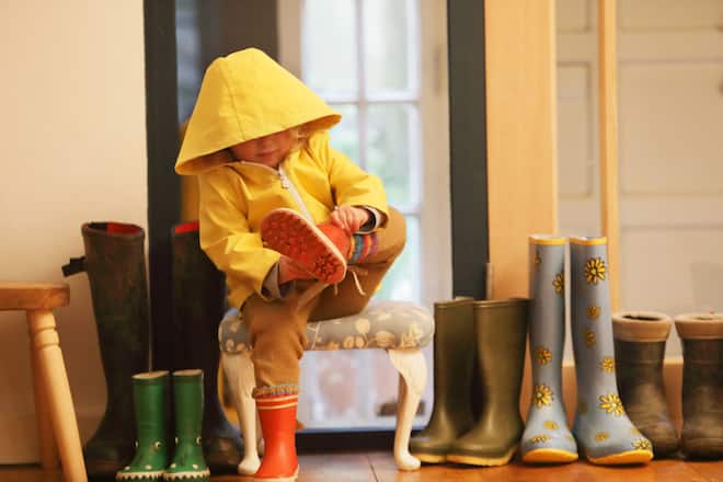 Kind in Regenmantel zieht zu Hause Gummistiefel aus