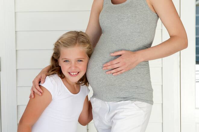 Mädchen hält Ohr an den Bauch seiner schwangeren Mutter