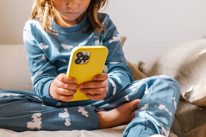 Creative Highlights Symbolbilder Cropped unrecognizable of girl in sleepwear playing game on cellphone while sitting on bed near window in light bedroom, Model released HodeiUnzueta_FraternalTwinsInPyjamas_19.jpg Copyright: xHodeixUnzuetax