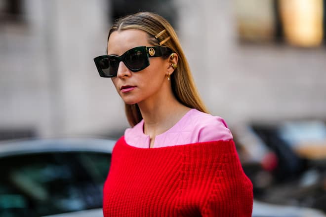 MILAN, ITALY - SEPTEMBER 22: Julia Comil wears black sunglasses, gold hair clips, gold earrings, a pale pink long midi dress, a red wool off-shoulder pullover, outside the Alberta Ferretti fashion show during the Milan Fashion Week - Spring / Summer 2022 on September 22, 2021 in Milan, Italy. (Photo by Edward Berthelot/Getty Images)