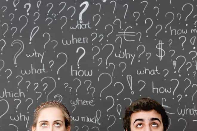 Young couple thinking in front of a blackboard filled with questions and question marks