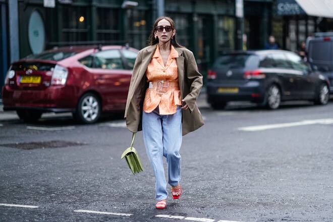 LONDON, ENGLAND - FEBRUARY 18: Chloe Harrouche wears a brown blazer jacket, an orange shirt, a large plastic tranparent belt, blue pants, a green bag, red shoes, sunglasses, during London Fashion Week February 2019 on February 18, 2019 in London, England. (Photo by Edward Berthelot/Getty Images)
