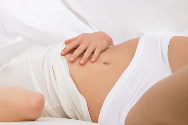 Woman laying in bed and touching her tummy.