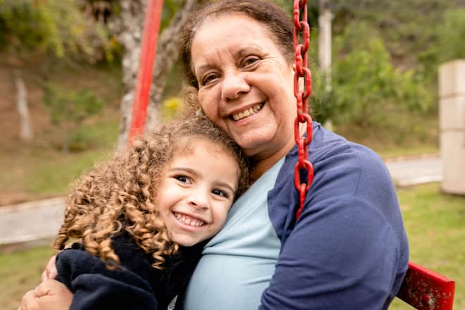Portrait of a smiling senior woman and her cute little granddaughter sitting together outside on a swing at home
