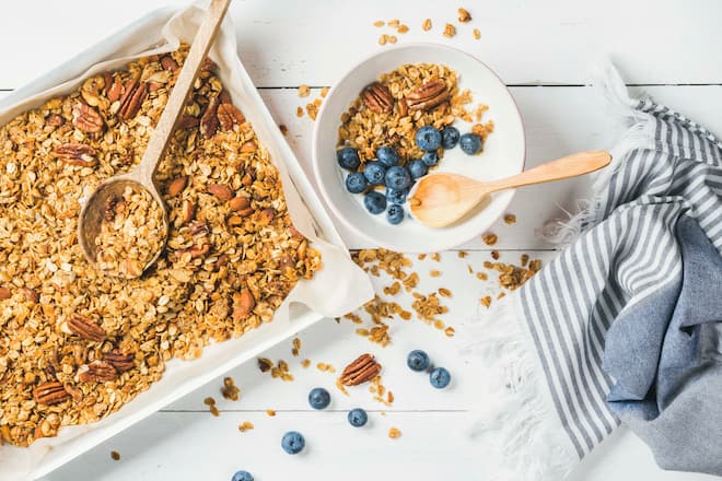 Healthy breakfast. Oat granola with pecan nuts, yogurt and blueberry in bowl on white wooden background, top view, vertical composition