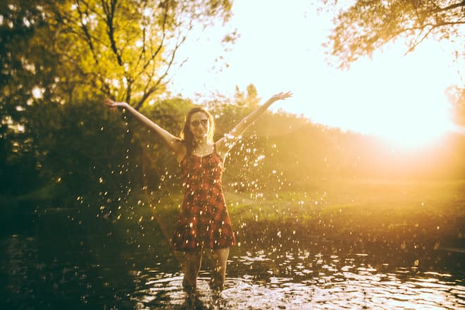 Young beautiful woman having fun in the river, splashing water on a sunny summer day.