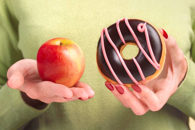A close up of a woman's hands, one holding an apple the other hand holding a doughnut