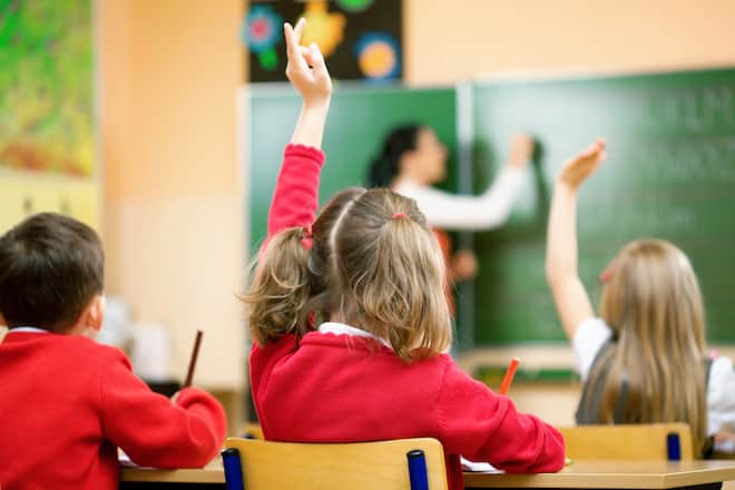 Elementary school kids raising their hands in class to answer a teacher's question.