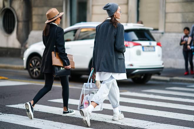 MILAN, ITALY - SEPTEMBER 19: A guest (L) wears a camel hat, a black jacket, black leggings, a black bag, a brown clutch, black sneakers ; A guest (R) wears a grey beanie hat, sunglasses, an oversized grey jacket, washed-out denim rolled-up hem baggy pants, light grey sneakers, a large transparent vinyl bag, outside the Bottega Veneta show during Milan Fashion Week Spring/Summer 2020 on September 19, 2019 in Milan, Italy. (Photo by Edward Berthelot/Getty Images)