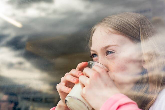 Girl (8-9) drinking milk, looking out of window