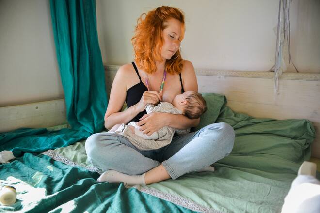Young mother breastfeeding her newborn at home on the bed
