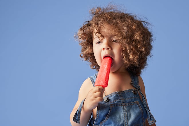 Unemotional thoughtful little girl standing with melting popsicle against blue background Copyright: xMathiasxAlvezx