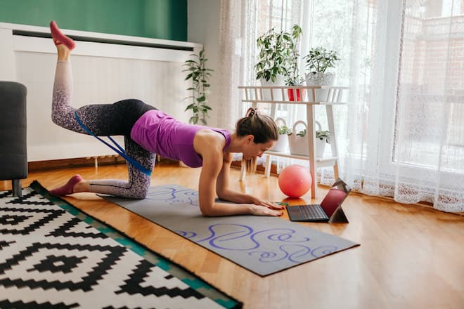 Fit woman works pilates and watching training videos on laptop.