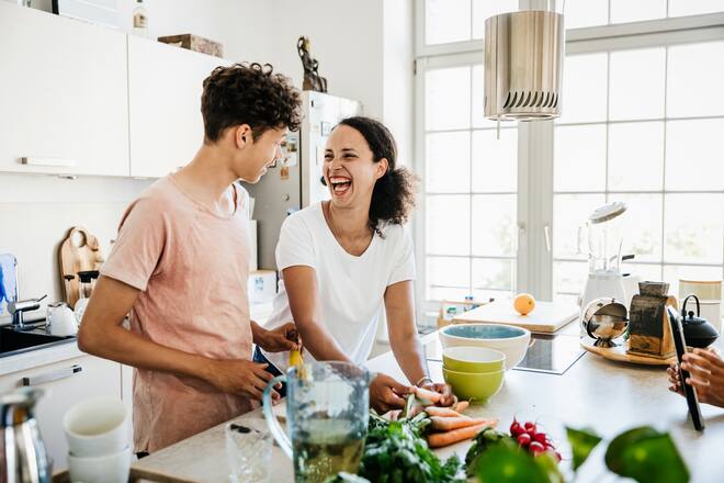 A single mom at home in the kitchen, laughing while preparing some lunch with her son.