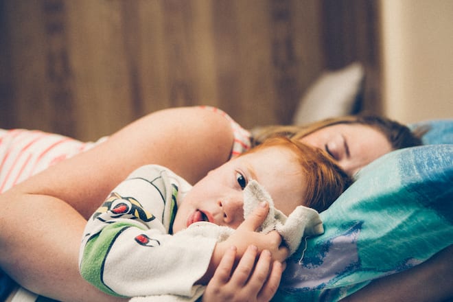 A mother sleeps while her cuddling her child, yet the son remains awake