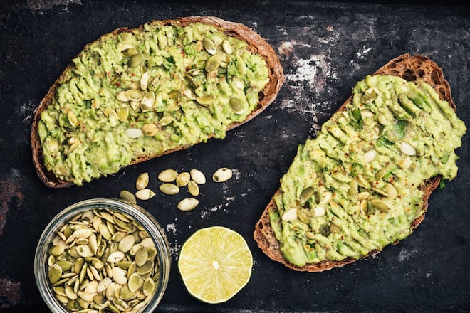 Two healthy rye bread toasts with mashed avocado, parsley and pumpkin seeds on black rusty background. Top view
