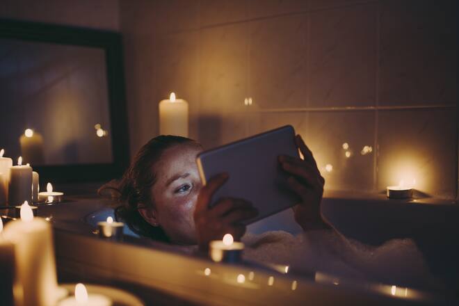 Smiling woman using tablet pc in bathtub with candles around.