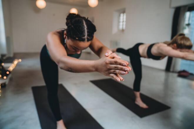 Young adult women together in warrior three pose at the yoga studio. Multi ethnic group.