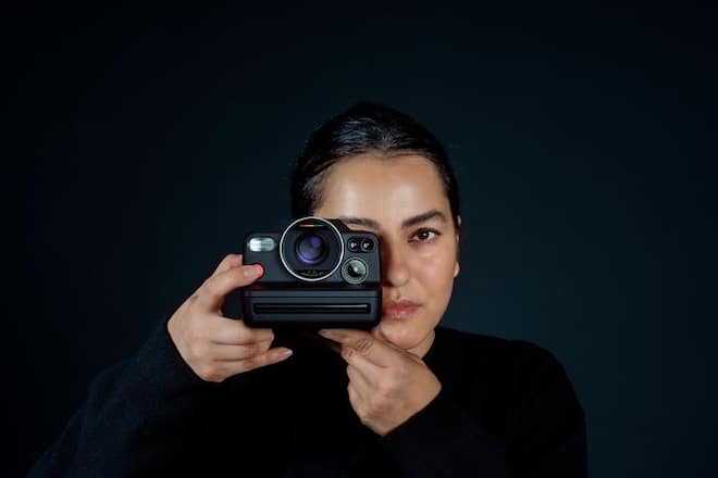 a woman with black hair holds a camera in front of her right eye