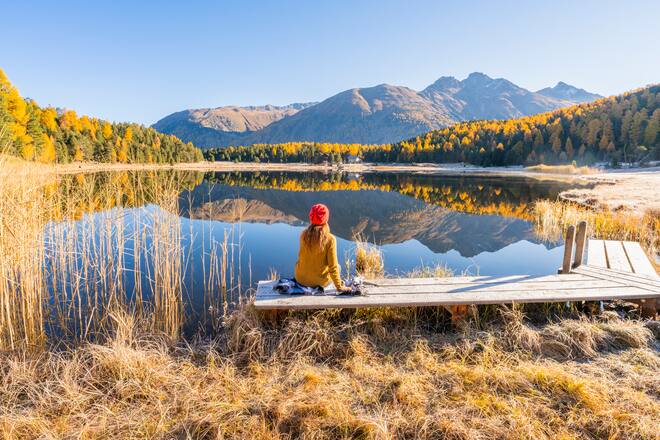 Rear view of a woman looking at view sitting on a boardwalk on Lake Staz. Celerina/Schlarigna, Maloja region, Canton of Grisons, Switzerland.